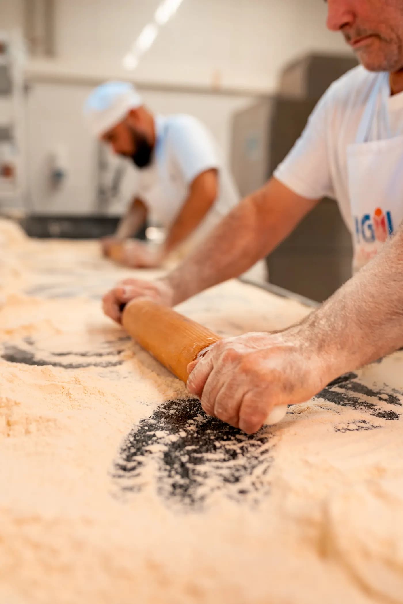 Bäcker rollt Teig mit dem Nudelholz auf dem bemehlten Tisch aus