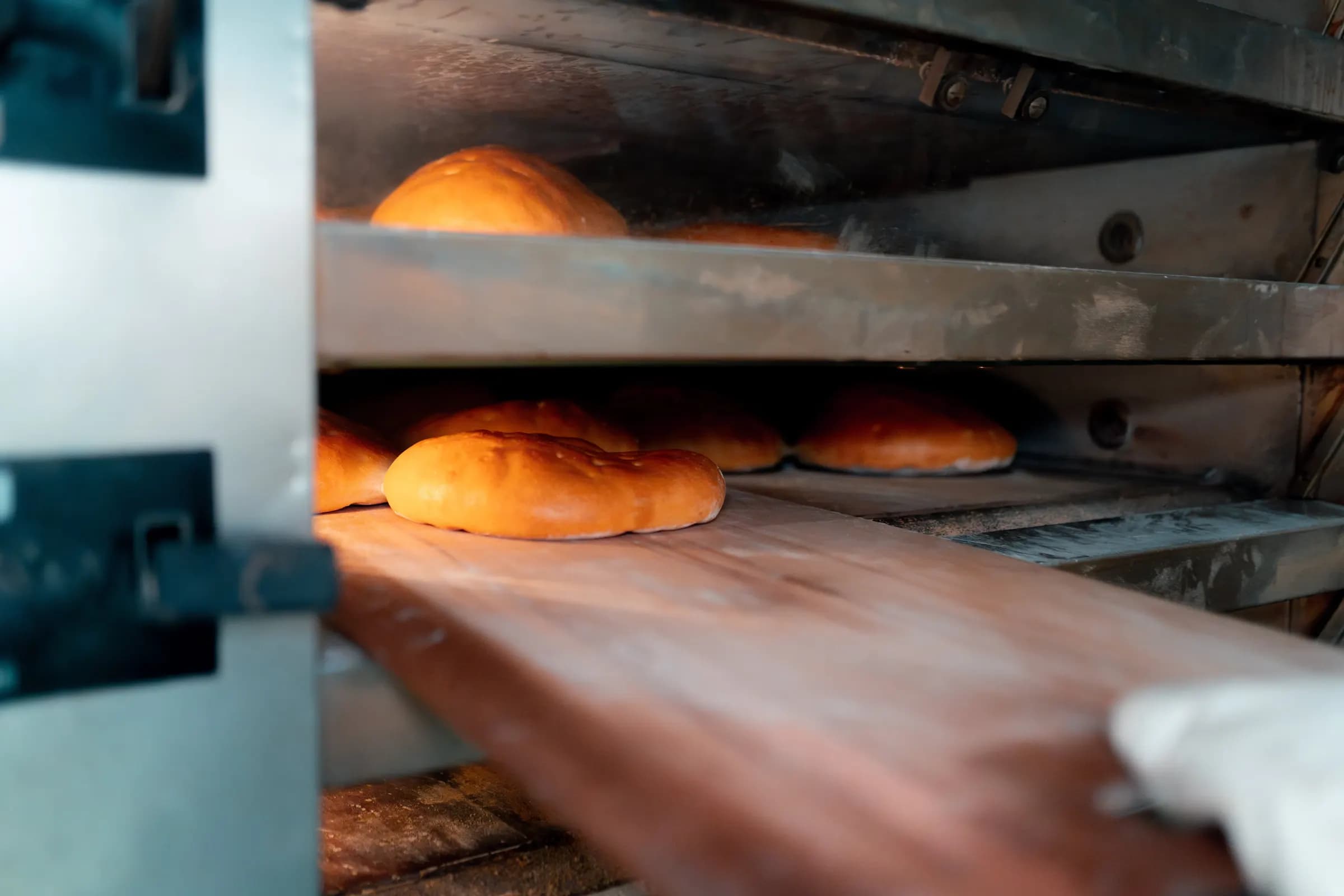 Frisch gebackene Fladenbrote im Etagenofen, ein Holzschieber holt sie heraus